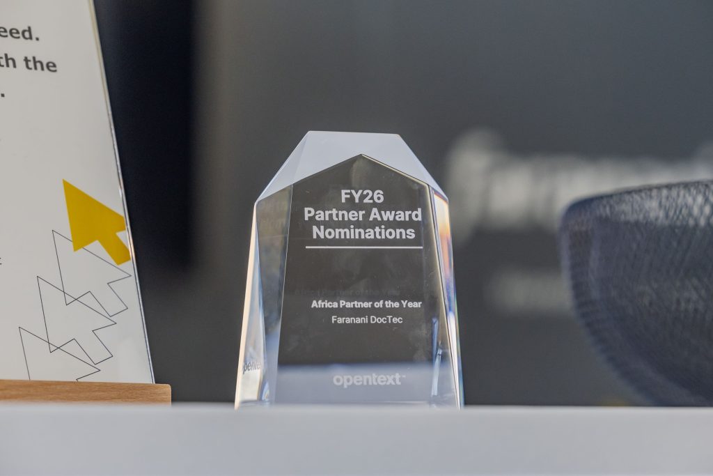 A photo of the crystal shaped and transparent OpenText Partner of the Year award for 2026 on an exhibition stand desk.